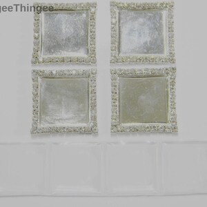 May include: Four square, clear glass trays with a silver, sparkly, rhinestone border. The trays are arranged in two rows of two. Below the trays is a long, rectangular, clear plastic tray.