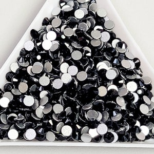 May include: A close-up of a pile of black and silver rhinestones in a white triangular tray.