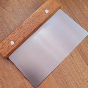 May include: A stainless steel pastry scraper with a wooden handle. The handle has two white metal rivets.