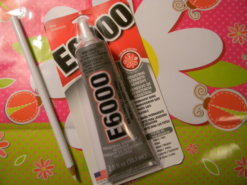 Pode incluir: Um tubo de adesivo industrial E6000, 59,1 ml, com um l&aacute;pis branco sobre um fundo com padr&atilde;o floral rosa e verde. O adesivo &eacute; n&atilde;o inflam&aacute;vel e adequado para tecido, madeira, vidro e cer&acirc;mica.