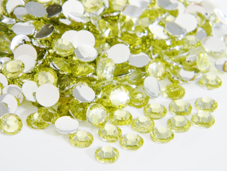 May include: A large pile of lime green rhinestones and round, silver-backed gems.