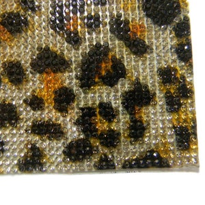 May include: Close-up of a leopard print fabric covered in small, clear, black, and amber rhinestones.