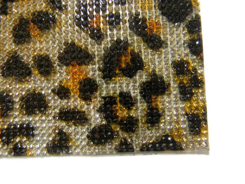 May include: Close-up of a leopard print fabric covered in small, clear, black, and amber rhinestones.