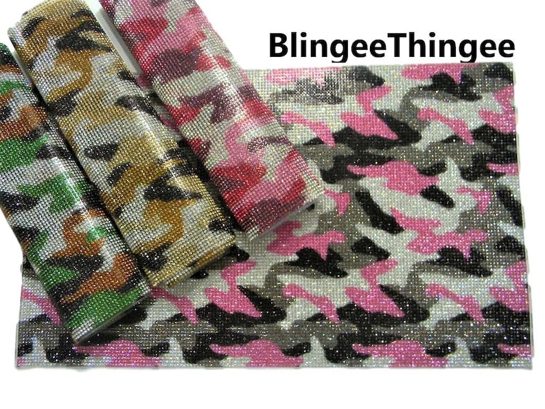 May include: Four rolls of rhinestone-covered fabric in camouflage patterns. The patterns include pink, green, black, and brown. The fabric is labeled "BlinggeeThinghee".