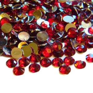 May include: A large pile of red and gold rhinestones. The rhinestones are scattered on a white background.