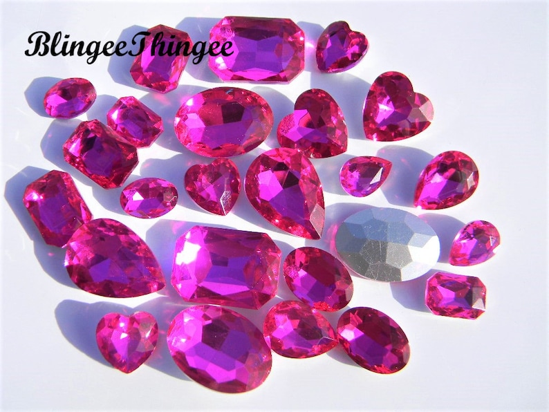 May include: Assortment of pink glass rhinestones in various shapes, including hearts, ovals, and rectangles.