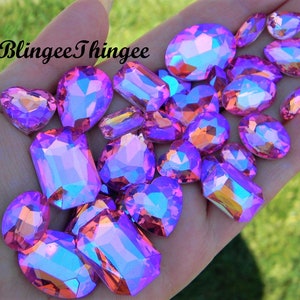Pode incluir: Conjunto de strass de vidro rosa e roxo iridescentes em vários formatos e tamanhos, incluindo ovais, retângulos e corações.