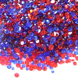 May include: A large pile of red and blue rhinestones, scattered on a white background. The rhinestones are small and round, and they are arranged in a random pattern.