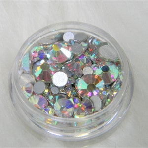 May include: A clear plastic container filled with iridescent rhinestones and silver-colored round embellishments.