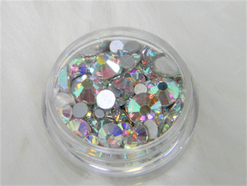May include: A clear plastic container filled with iridescent rhinestones and silver-colored round embellishments.