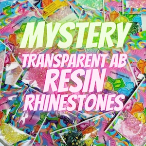 May include: A variety of small, clear, iridescent resin rhinestones in different colors are packaged in small, colorful bags with the text "Bling" and "Sparkly Supply Shop". The bags are stacked on top of each other. The text "MYSTERY TRANSPARENT AB RESIN RHINESTONES" is superimposed on the image.