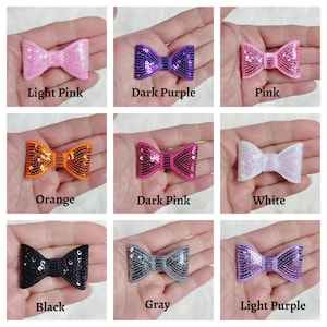 Peut inclure: Assortiment de dix pinces à cheveux en forme de nœud pailletées dans différentes couleurs, notamment rose clair, violet foncé, rose, orange, rose foncé, blanc, noir, gris et violet clair.