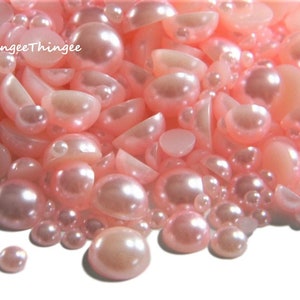 May include: A large assortment of pink pearl-like embellishments in various sizes and shapes. The embellishments are scattered on a white background.