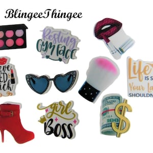 May include: Nine colorful, round, printed stickers with various beauty and fashion related themes. The stickers feature phrases like "Resting Gym Face", "I believe in red lipstick", "Life is short your lashes shouldn't be!" and "Girl Boss".