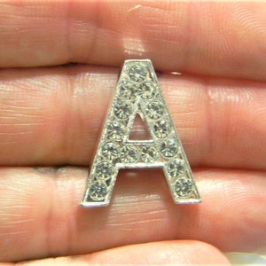 Pode incluir: Um charme de letra A prateado com strass transparentes.