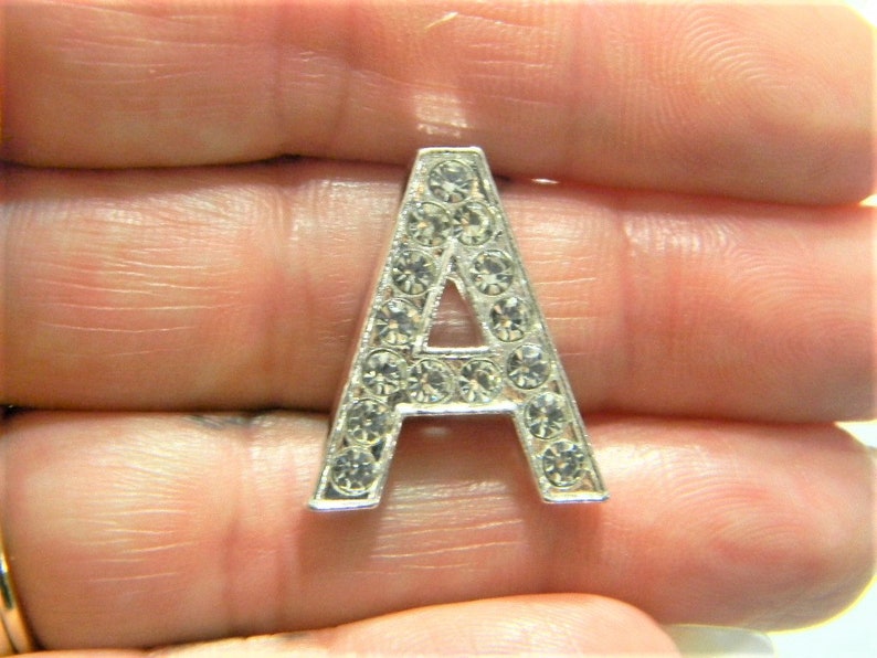 Pode incluir: Um charme de letra A prateado com strass transparentes.