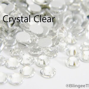 May include: A close-up image of a pile of clear crystal rhinestones. The rhinestones are small and have a faceted design. The text "Crystal Clear" is visible in the image.