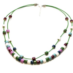 May include: A layered necklace with a green cord and colorful cylindrical beads. The beads are in shades of white, blue, green, purple, and burgundy. The necklace has a silver-toned clasp.