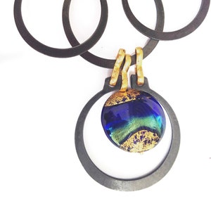 May include: A handcrafted necklace featuring a dark metal chain with interlocking oval and circular links. The pendant showcases a blue and green glass orb with gold accents, suspended within a circular frame.