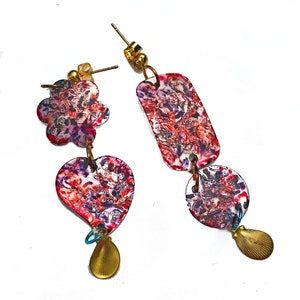 May include: A pair of mismatched earrings with floral and geometric shapes. One earring features a flower and heart, the other a rectangle and circle. The earrings have a red, purple, and white floral pattern with gold-colored accents.