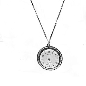 May include: A silver-toned pocket watch pendant with a chain. The watch face is white with black numerals and hands, and the text "SUPER LUXE" is visible. The watch has a small seconds dial and a decorative bezel.