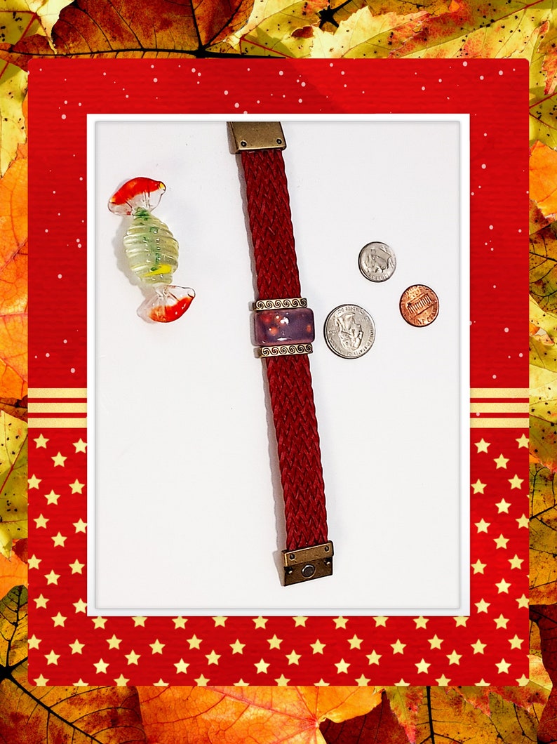 May include: A braided burgundy bracelet with a rectangular purple centerpiece, accented with bronze-colored metal. A glass candy and three coins are also present. The bracelet is approximately 7 inches long.
