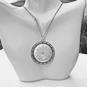 May include: A silver-toned pendant necklace featuring a repurposed vintage watch face. The watch face displays the time and the words "SUPER LUXE". The necklace is displayed on a white mannequin bust.