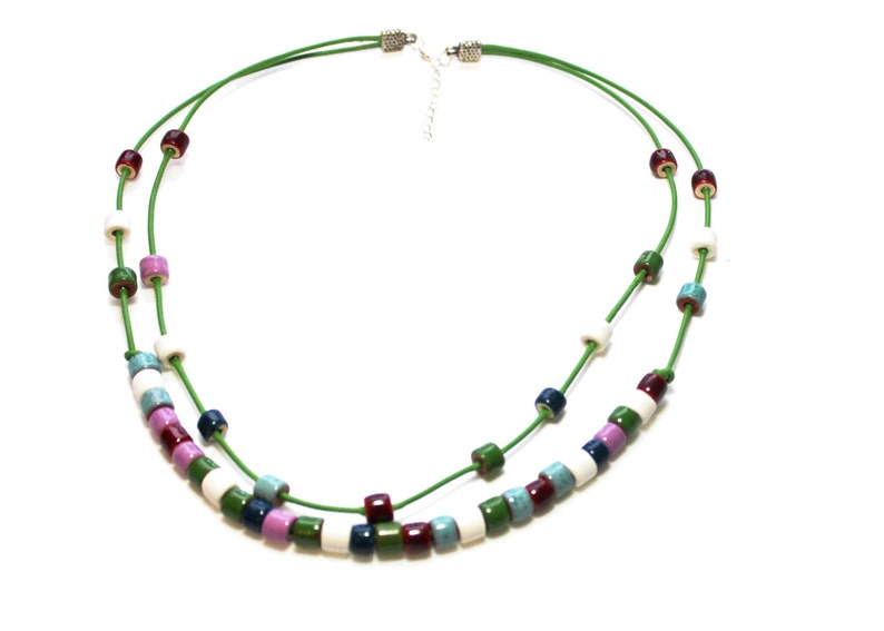 May include: A layered necklace with a green cord and colorful cylindrical beads. The beads are in shades of white, blue, green, purple, and burgundy. The necklace has a silver-toned clasp.