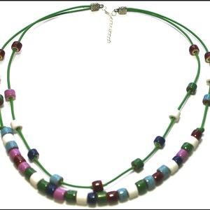 May include: A two-strand necklace with a green cord and colorful cylindrical beads. The beads are in shades of white, blue, pink, green, and burgundy. The necklace has a silver-toned clasp and extender chain.