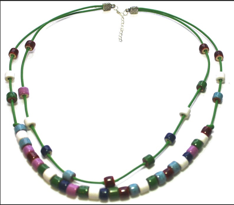 May include: A two-strand necklace with a green cord and colorful cylindrical beads. The beads are in shades of white, blue, pink, green, and burgundy. The necklace has a silver-toned clasp and extender chain.