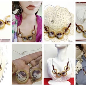 May include: A necklace featuring a series of circular horn-colored rings, interspersed with small dark red beads and two central circular pendants decorated with a white and dark brown swirl pattern, all strung on a thin silver-toned wire cord.