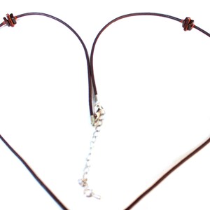 May include: A necklace with a dark brown cord and decorative beads. The beads include purple, brown, and orange elements. The necklace has a silver-colored clasp and a chain for adjusting the length.