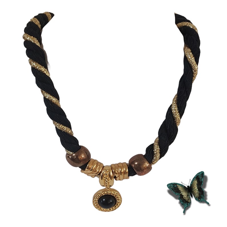 May include: Black and gold rope necklace with a gold pendant featuring a black stone. The necklace has gold accents and bronze-colored beads. A decorative butterfly is next to the necklace.