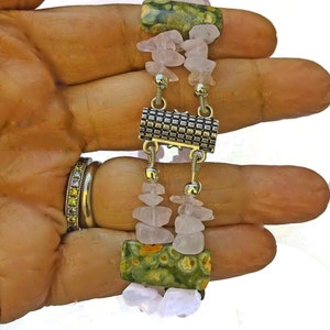May include: A handmade bracelet featuring alternating sections of light pink rose quartz chips and green jasper stones. The bracelet is connected with silver-toned metal links and a decorative clasp.