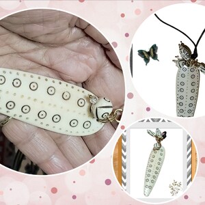 May include: Ivory-colored pendant necklace with a black cord. The pendant is elongated with a series of small, dark circles and a decorative bead. A butterfly is near the pendant. The necklace is handmade.