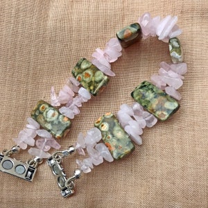 May include: A handmade bracelet featuring a combination of rose quartz chips and rectangular leopard jasper stones. The bracelet is secured with a silver magnetic clasp. The rose quartz chips are a soft pink color, and the jasper stones have green and brown patterns.