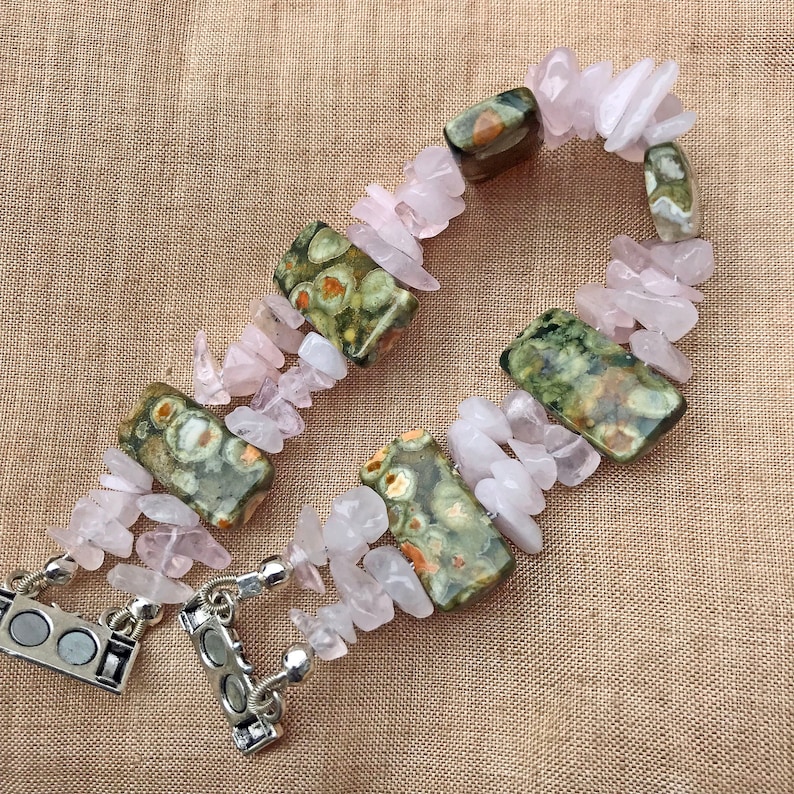 May include: A handmade bracelet featuring a combination of rose quartz chips and rectangular leopard jasper stones. The bracelet is secured with a silver magnetic clasp. The rose quartz chips are a soft pink color, and the jasper stones have green and brown patterns.