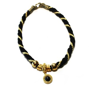 May include: A black and gold rope necklace with a gold clasp. The necklace features a gold pendant with a black stone. The rope is twisted with gold thread.