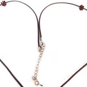 May include: A brown leather necklace with decorative beads. The necklace features square and round beads in shades of purple, red, and brown. The necklace has a silver-colored chain for adjustable length.