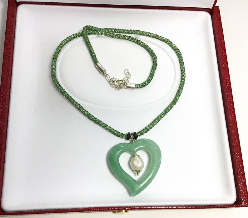 May include: A green jade heart pendant necklace with a pearl accent. The necklace is on a green beaded chain and is displayed in a red velvet jewelry box.
