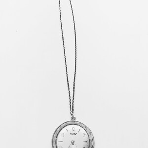 May include: A vintage pocket watch with a silver-tone case and a white face, suspended from a delicate chain. The watch face features black numerals and hands, with a smaller subdial. The watch is a classic accessory.