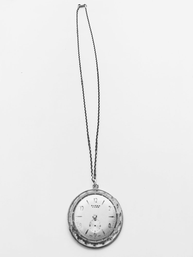 May include: A vintage pocket watch with a silver-tone case and a white face, suspended from a delicate chain. The watch face features black numerals and hands, with a smaller subdial. The watch is a classic accessory.