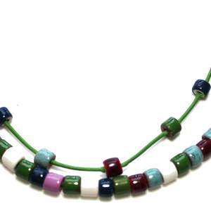 May include: A colorful necklace featuring small, square beads in various colors including white, green, purple, blue, and burgundy. The beads are strung on a bright green cord, creating a vibrant and eye-catching accessory.