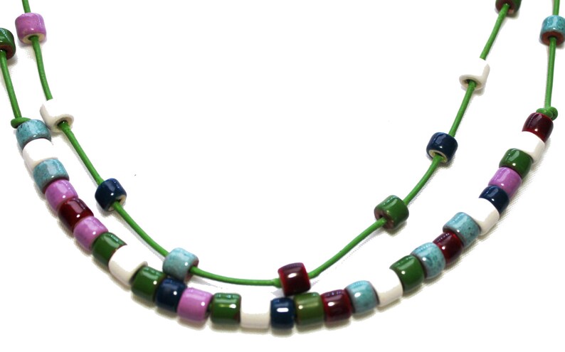 May include: A colorful necklace featuring small, square beads in various colors including white, green, purple, blue, and burgundy. The beads are strung on a bright green cord, creating a vibrant and eye-catching accessory.