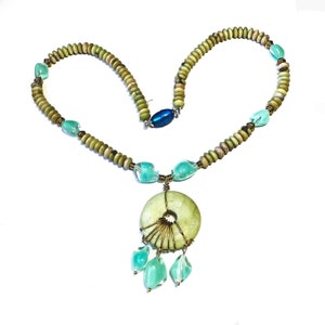 May include: A handcrafted necklace featuring a light green circular pendant with wire detailing and dangling aqua-colored teardrop-shaped beads. The necklace includes light green and tan-colored beads, aqua-colored accent beads, and a blue clasp.