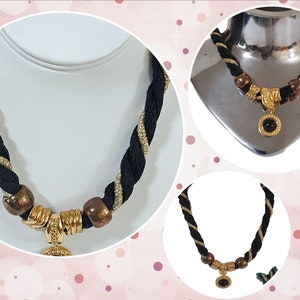 May include: A black and gold rope necklace with gold-toned accents and a circular pendant with a black stone. The necklace features a braided design with gold metallic thread woven into the black rope.