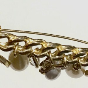 May include: Backside view of a gold-toned brooch with a chain design and dangling faux pearls. The pin has a safety clasp. The text "Pin Backside Shrishti" is visible.