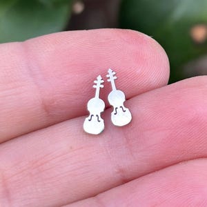 May include: A pair of silver violin-shaped stud earrings. The earrings are small and delicate, and they would make a great gift for a musician or music lover.