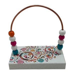 May include: A wooden toy with a colorful design and a copper wire archway. The archway has a string of colorful beads that can be moved up and down.