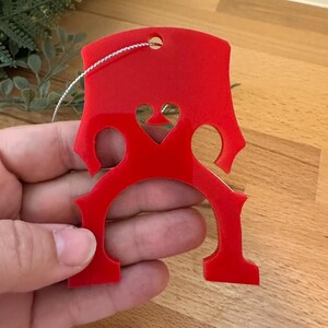 Könnte beinhalten: Roter Acryl-Weihnachtsbaumschmuck in Form eines Bassschlüssels mit einem ausgeschnittenen Herzen in der Mitte.